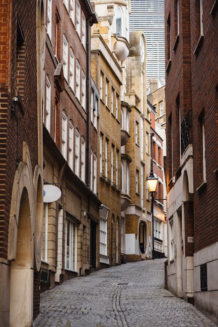 A narrow residential street in Belgravia, Westminster, with tall, multi-storey brick and white-painted buildings on both sides. The street is paved with cobblestones and lined with black bollards. The