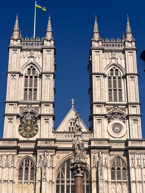 The image depicts the façade of Westminster Abbey, a historic Gothic church with two prominent square towers topped with spires and intricate stone carvings. The twin towers feature large arched wind