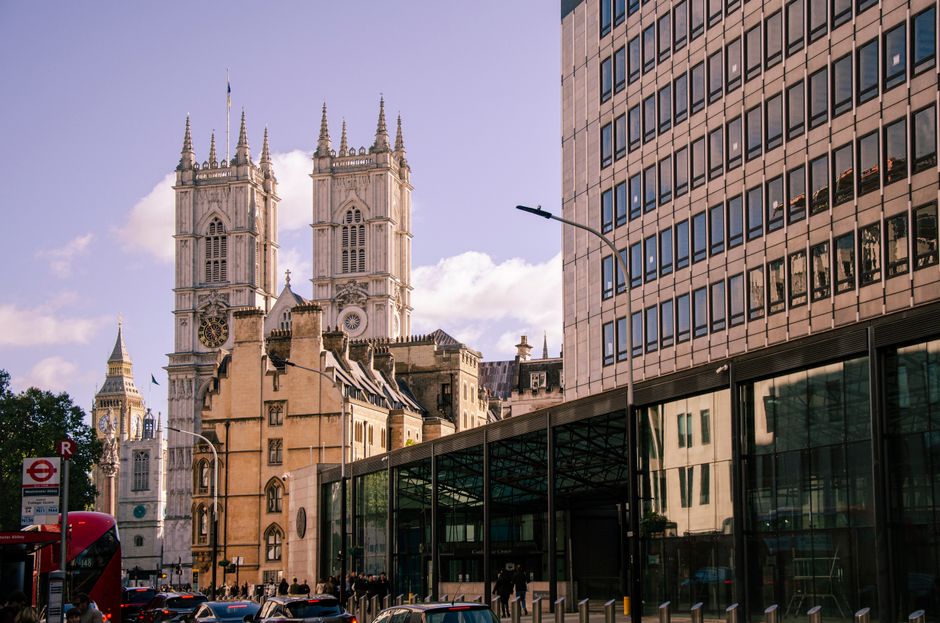 The image depicts the façade of Westminster Abbey, a historic Gothic church with two prominent square towers topped with spires and intricate stone carvings. The twin towers feature large arched wind